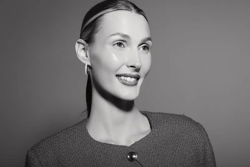 Smiling Caucasian woman with light skin and sleek hair poses wearing a textured top against plain background. Concept of happiness and elegance.