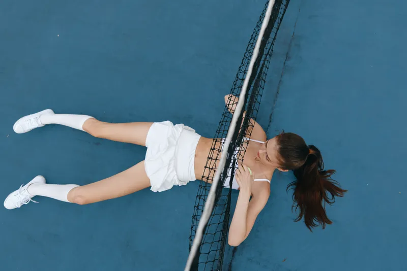 Young female athlete in white sportswear lying on a tennis court, expressing determination, during an intense training session