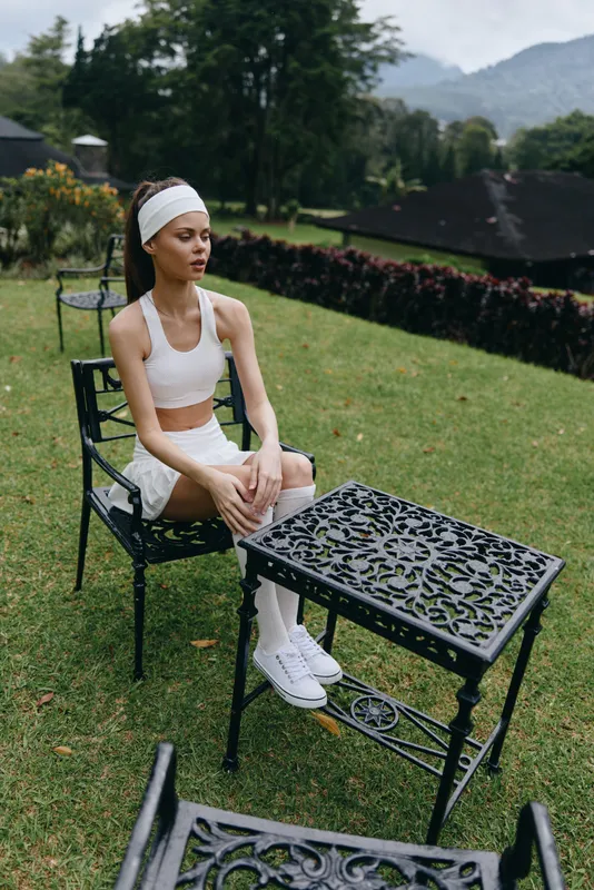 Young Asian woman in sporty outfit enjoying peaceful yoga moment outdoors, surrounded by lush greenery and elegant outdoor furniture