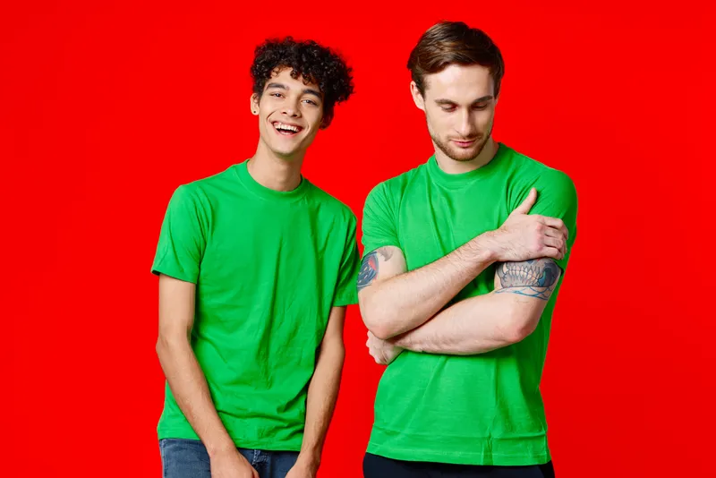 Радостные друзья в зеленых футболках стоят рядом с красным фоном