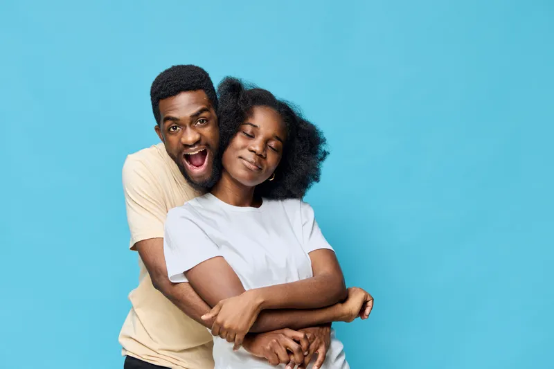 Happy young couple embracing each other against a blue background, showcasing love and joy, perfect for seasonal themes and relationship concepts