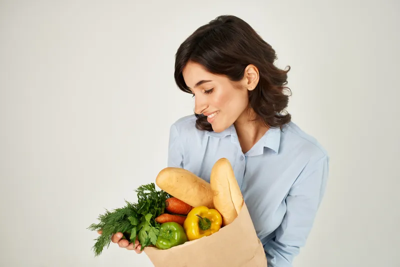 Женщина в голубой рубашке с пакетом овощей и продуктов