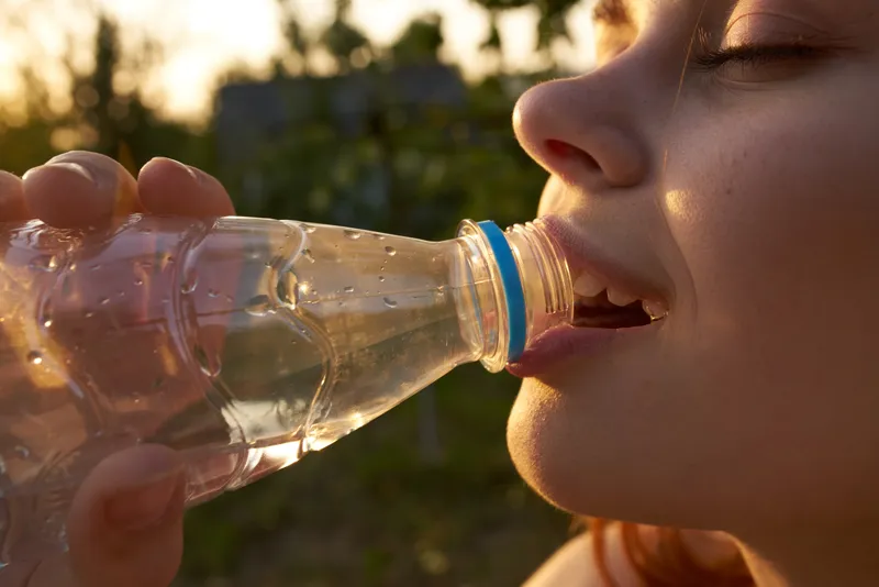 Веселая женщина пьет воду из бутылки летом, крупный план