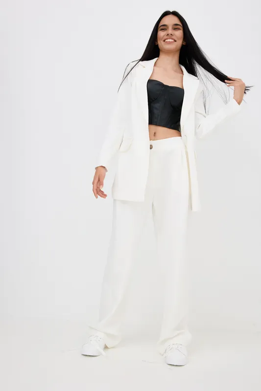 smiling woman in stylish white suit and black crop top posing confidently against a light background, showcasing modern fashion and youthful energy.
