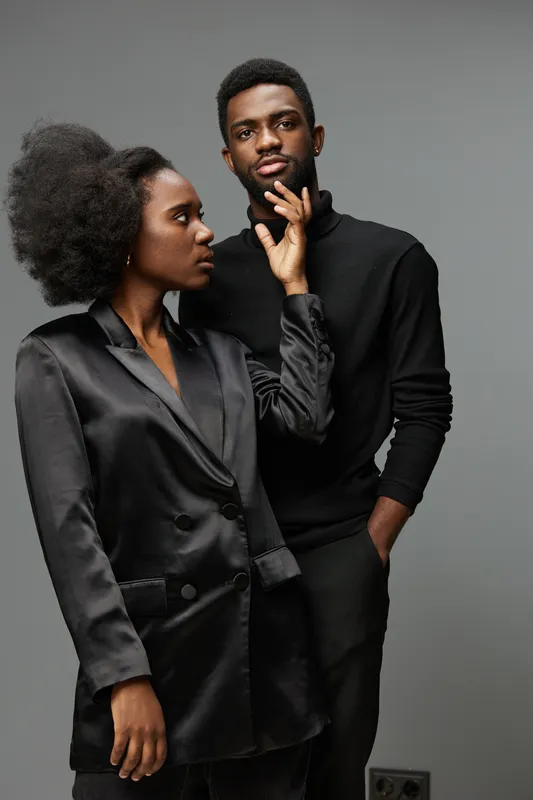 Portrait of a stylish Black couple with an elegant, moody aesthetic, showcasing confidence and connection against a neutral backdrop