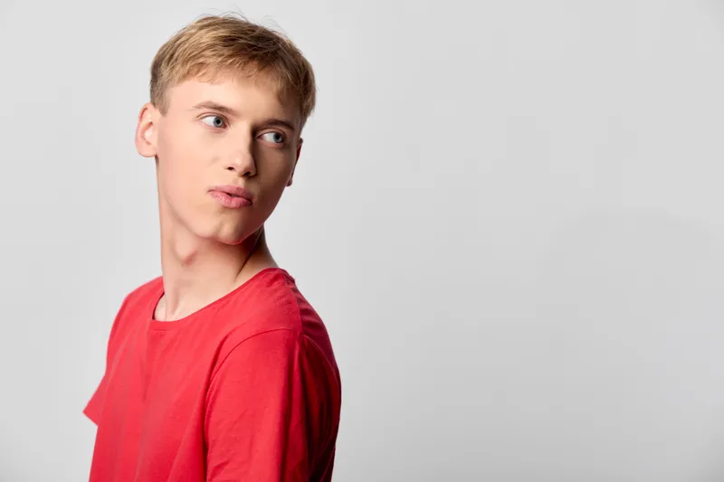 Young man in red shirt looks to the side with a thoughtful gaze in a clean studio, conveying curiosity, mood, and calm confidence for lifestyle and entertainment projects
