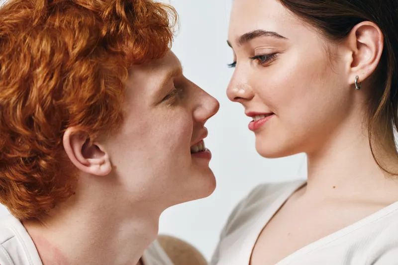 Couple, young man and woman, closeup portrait with red hair and smile, looking at each other with affection and tenderness on white background in studio.