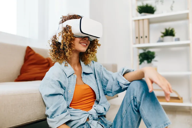 Улыбающаяся женщина наслаждается игрой в виртуальную реальность дома с футуристическими VR-очками и контроллером