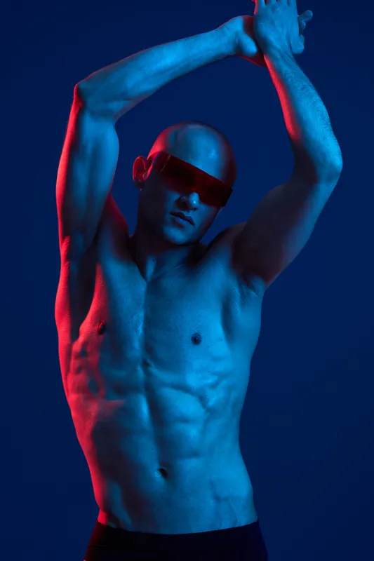 Athletic man posing dramatically under vibrant blue and red lights, showcasing strength and physique in an artistic display, perfect for fitness concepts.