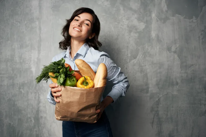 На фотографии высокого качества изображена женщина с пакетом продуктов в супермаркете, что символизирует здоровое питание и качественное обслуживание