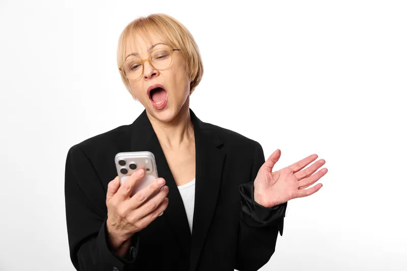 Businesswoman holding smartphone, surprised shocked expression, mouth open hand gesture, blazer and glasses, isolated on white background, mobile communication stress concept