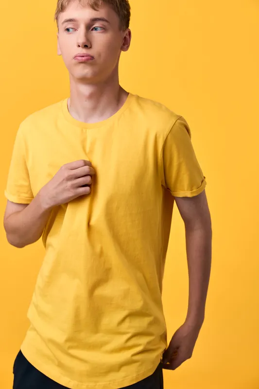 Young man in a bright yellow shirt poses against a yellow background, showcasing casual wear and a confident stance in studio lighting