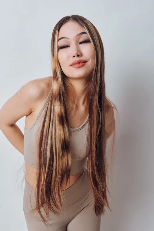 Young woman with long straight hair posing in beige sportswear against a plain background. Casual confident female model with natural makeup and relaxed expression in studio.