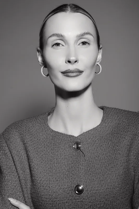 Elegant slim white woman with pale skin and slicked back hair wearing hoop earrings and textured jacket poses confidently in studio. Concept of fashion, beauty, and strength.