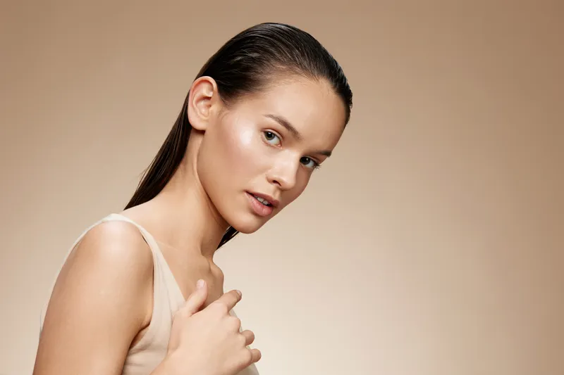 Elegant portrait of a young model with smooth skin and wet hair against a soft beige background, showcasing natural beauty and simplicity