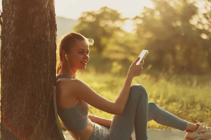 Young woman enjoying music outdoors on a sunny day, wearing casual clothing, creating a relaxed and joyful atmosphere in nature