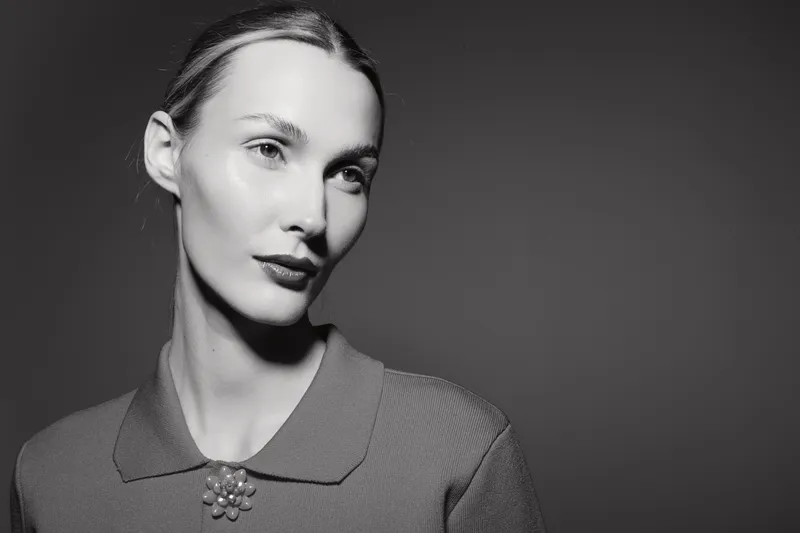 Portrait of a fair skinned Caucasian woman with slicked back hair and vintage style blouse in black and white studio lighting.