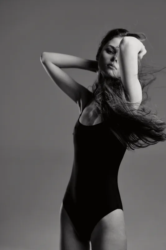 Black and white portrait of a graceful woman posing in a sleeveless bodysuit with flowing hair and soft expression.
