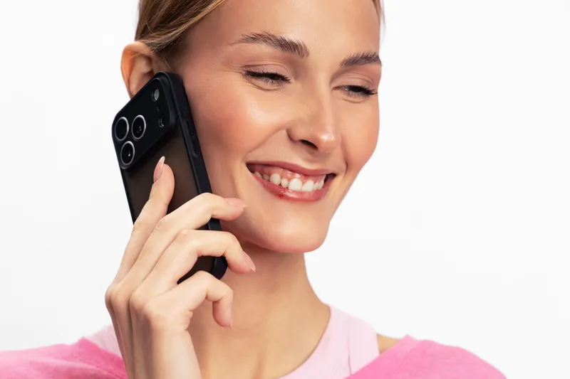Smiling woman with clear skin holding smartphone near ear in studio on white background. Concept of communication, happiness, technology, connection, and positive mood in everyday life.