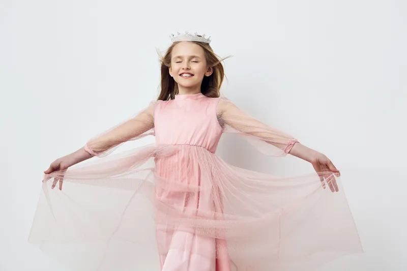 Happy girl in a pink dress with tulle, smiling and playing against a light background, ideal for children s fashion and joyful moments