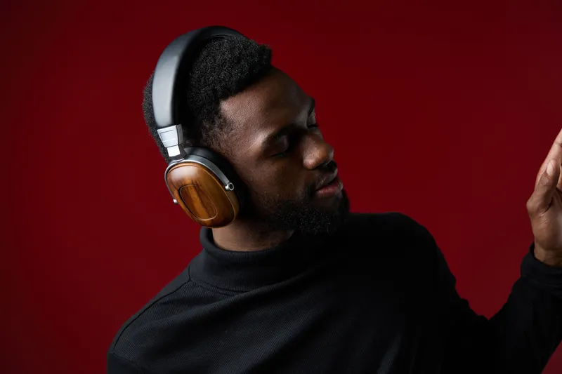 A stylish Black man enjoying music with wooden headphones against a rich red background, showcasing a relaxed and joyful emotion that represents modern lifestyle and music culture