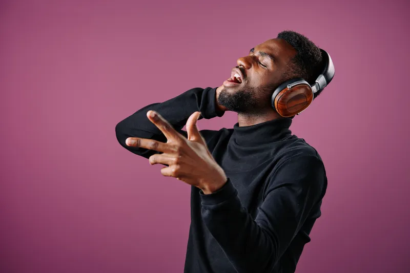 A joyful Black man enjoying music while wearing headphones against a vibrant pink background, expressing emotion and energy through his movements, perfect for music and lifestyle themes