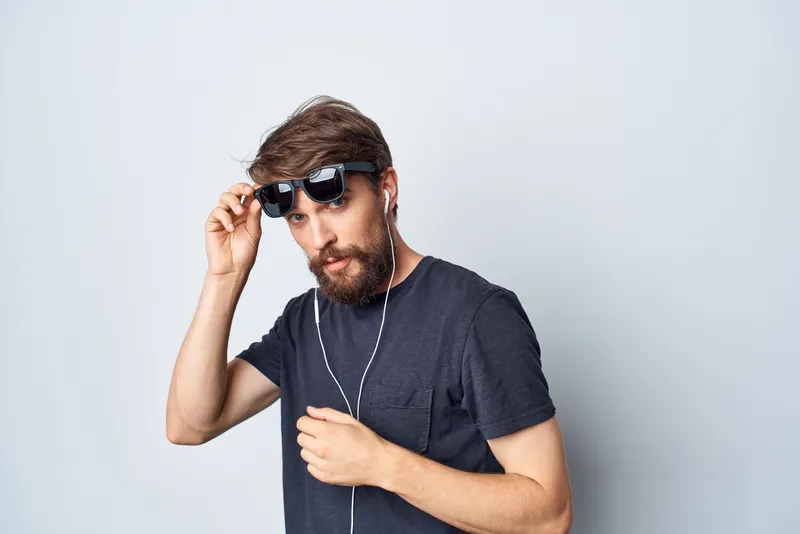 Красивый мужчина в черной футболке слушает музыку в наушниках, двигаясь на светлом фоне