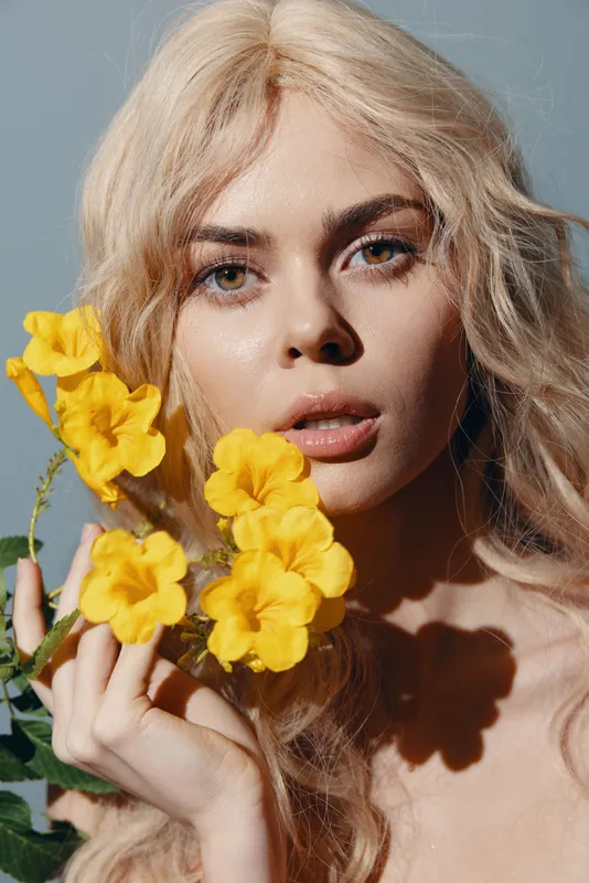 Откройте для себя элегантность молодой женщины с распущенными светлыми волосами, которая нежно держит яркие желтые цветы