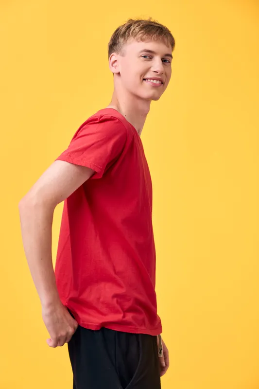 Man in a red t shirt stands against a bright yellow backdrop, smiling and relaxed, showcasing casual fashion and upbeat lifestyle vibe suitable for youth campaigns and product showcases