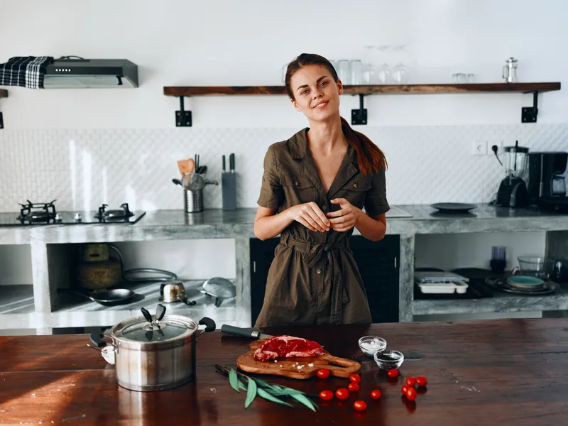 Женщина улыбается на кухне, готовит еду, используя мясо и овощи