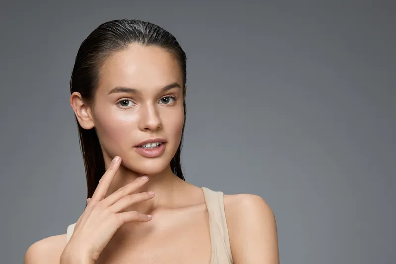 Natural beauty portrait of an Asian female model with wet hair, neutral expression, and soft skin tones against a gray background, perfect for beauty and skincare concepts