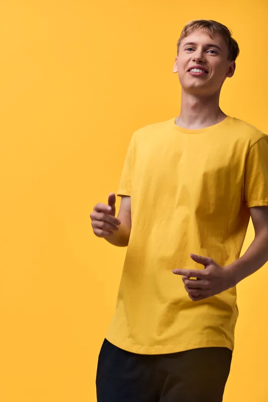 Smiling man in a yellow shirt against a yellow background in a studio setting with a bright color palette, relaxed pose and casual clothing, conveying a cheerful expression and youthful style for