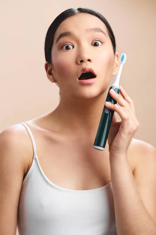 asian woman is surprised while holding a toothbrush beside her ear in a bright bathroom, creating a playful, everyday health moment with a modern lifestyle vibe.