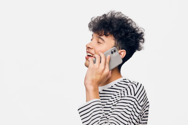 young man talking on smartphone in striped shirt smiling happily, isolated on white background, casual communication and modern lifestyle concept