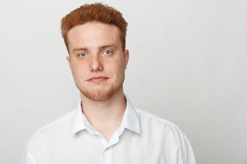 Portrait of a young man with red hair and beard wearing a white shirt against a plain light background. Concept of casual style, confidence, and natural appearance.