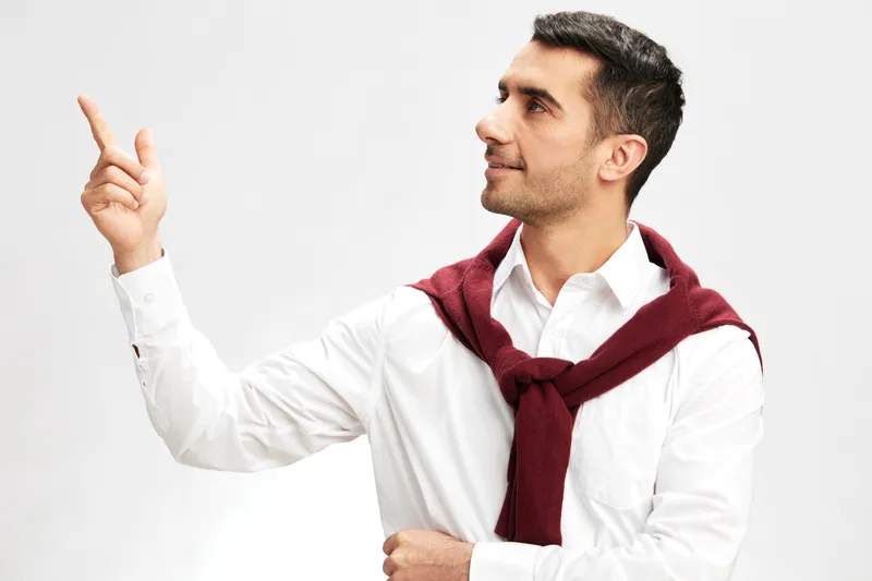 Красивый мужчина в белой рубашке со свитером на плечах, задумчивый взгляд