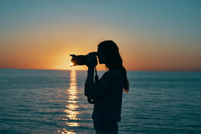 Женщина-фотограф с камерой на закате у моря, на пляже