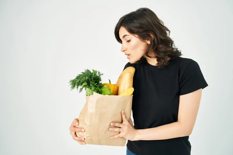 Брюнетка в черной футболке держит пакет с продуктами из супермаркета для доставки