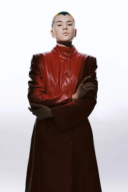 confident woman in red leather coat stands with crossed arms against bright background showcasing modern fashion and bold attitude in minimalistic style.