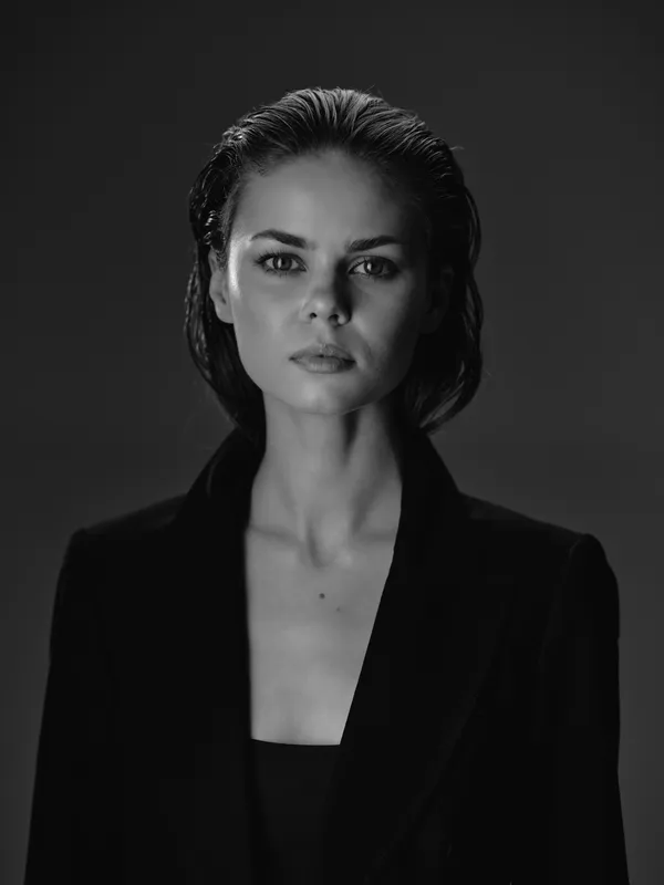 Black and white portrait of a serious woman with wet hair wearing a dark jacket in studio lighting.