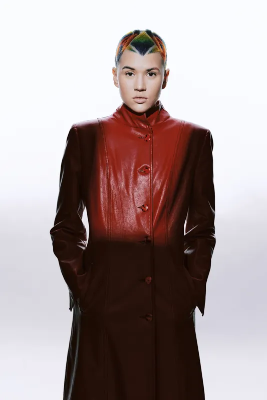 young woman with colorful hair wearing a red leather coat stands confidently against a white background, showcasing modern fashion and unique style