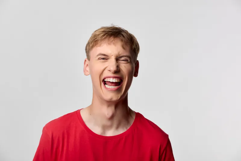 Loud laugh and shouting man in red shirt expressing high energy and joy, dynamic facial expression in studio setting, candid moment of exuberant emotion and playful mood