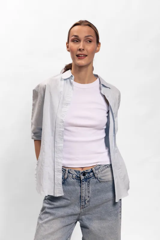 Young woman wearing casual light shirt and white top stands posing with hands behind back on white background. Concept for fashion, lifestyle, confidence, and casual style.