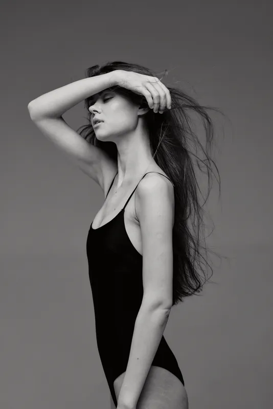 Black and white portrait of a slender woman in a black bodysuit with long hair and a serene expression