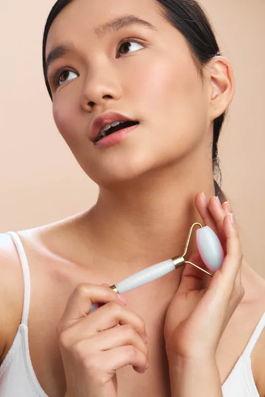 asian woman using a facial tool in a soft studio setting, focusing on skincare and relaxation, creating a calm, wellness mood.