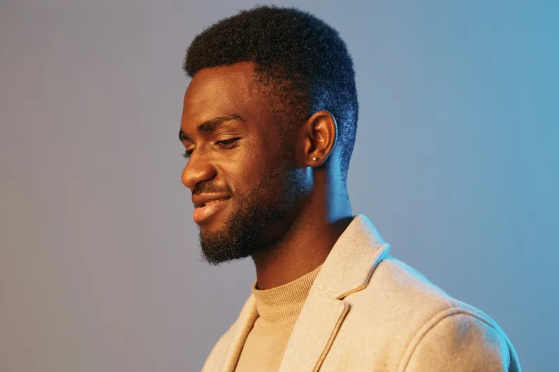 Smiling young Black man in a stylish beige blazer, captured with vibrant blue background, showcasing a confident and relaxed expression in a modern setting
