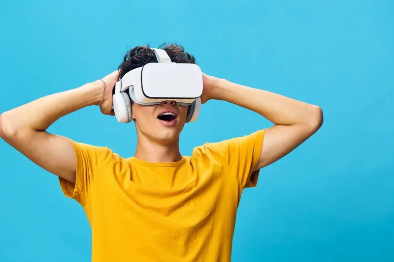 Взволнованный молодой человек в VR-гарнитуре и наушниках, демонстрирующий захватывающий опыт виртуальной реальности