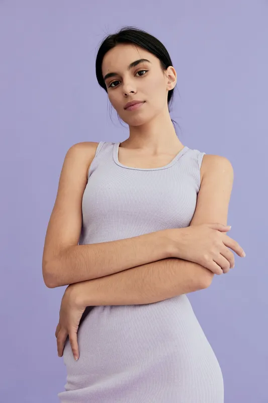 Young woman in lavender sleeveless dress posing with folded arms against purple background, displaying calm expression and minimalistic style.
