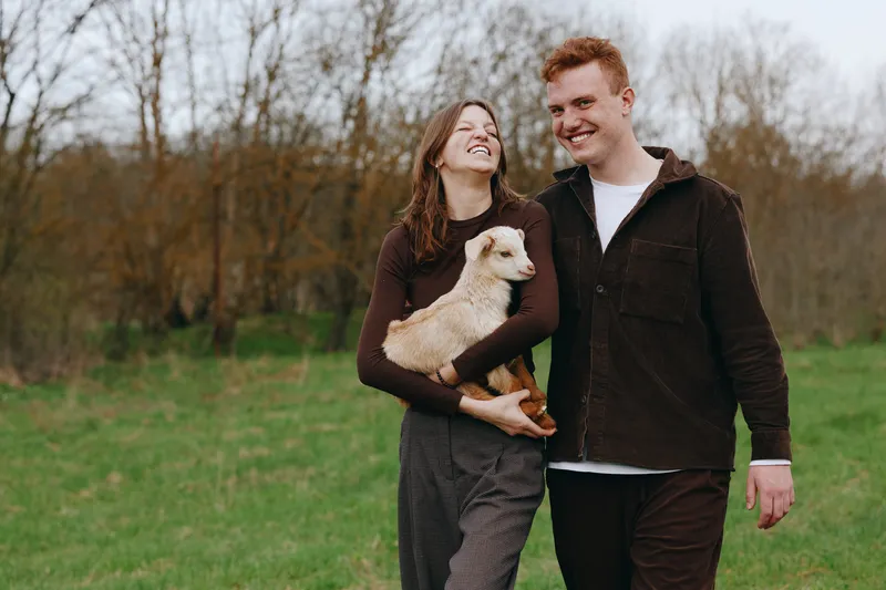 Smiling couple walks through a park with a small dog, enjoying a carefree autumn afternoon, casual outfits, warm connection, candid moment, natural light, lifestyle portrait, joyful atmosphere