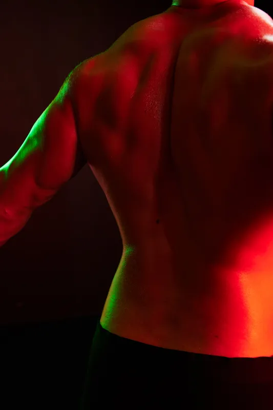 Мужчина-бодибилдер, спортсмен с обнажённым торсом в спортивной форме, изолирован на чёрном фоне в неоновом свете